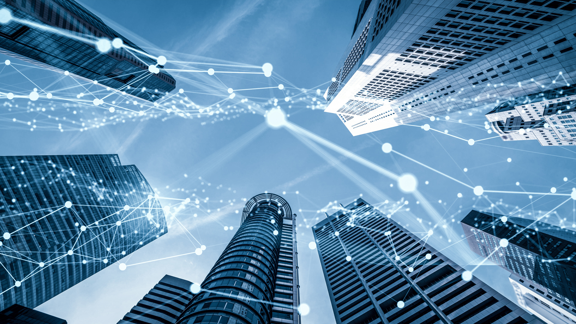 A view looking up between tall skyscrapers with a blue sky above. There are digital connecting lines and nodes overlaying the buildings, symbolizing technology and connectivity in an urban environment.