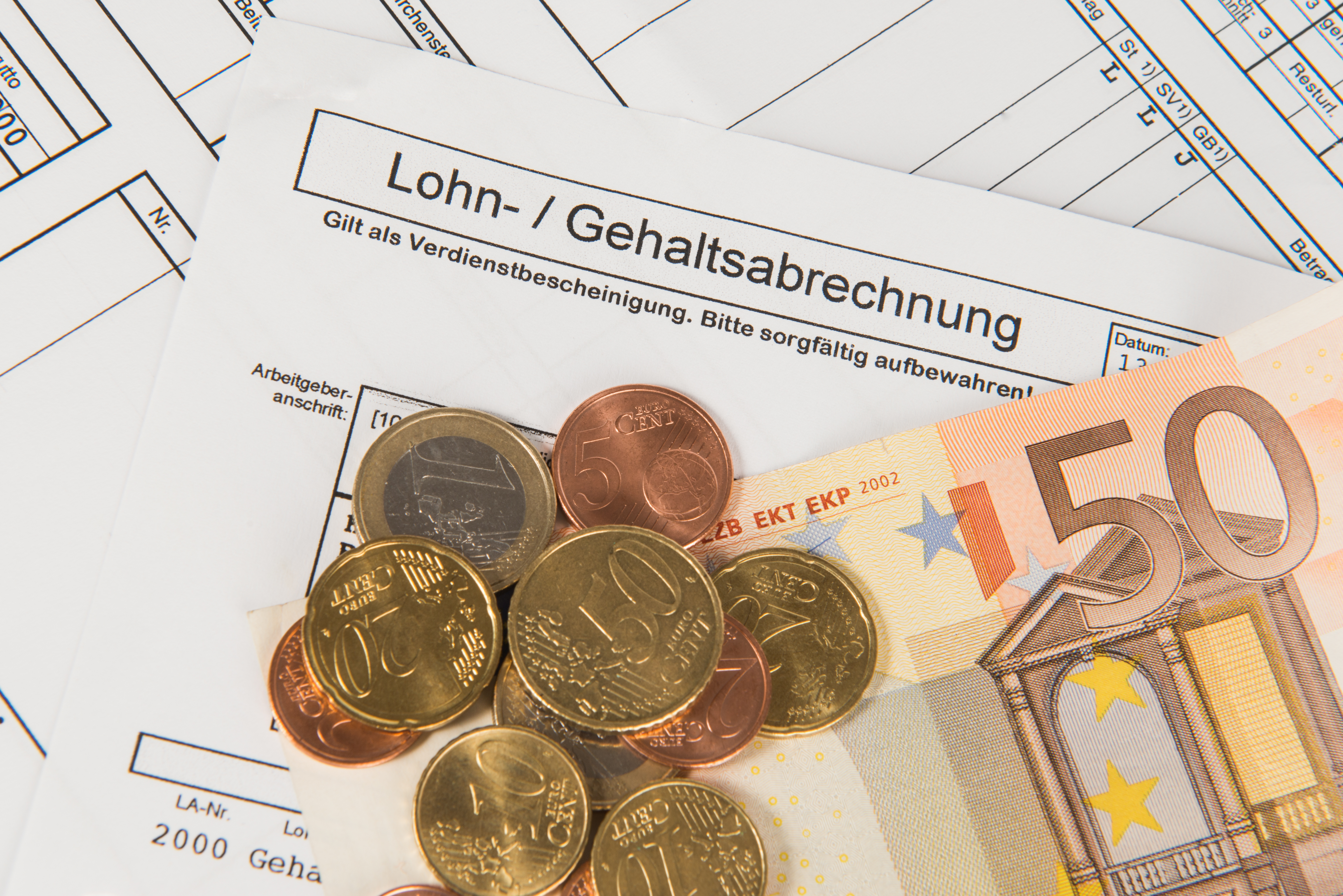 An image of a payment statement titled "Lohn- / Gehaltsabrechnung" with various coins and a 50 Euro banknote placed on it. The image highlights the financial documents and currency, emphasizing the theme of income or salary.